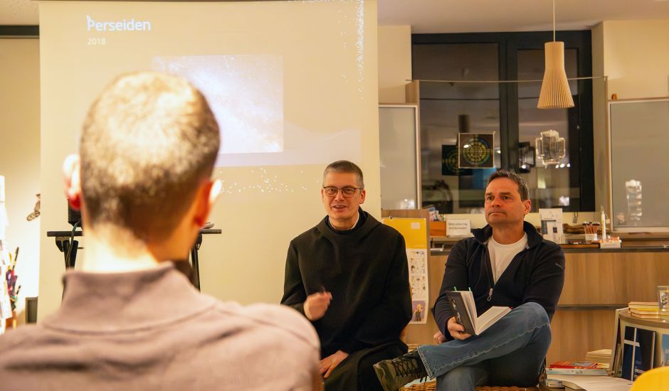 Mann im Habit und Mann in Alltagskleider sitzen in einem Buchladen