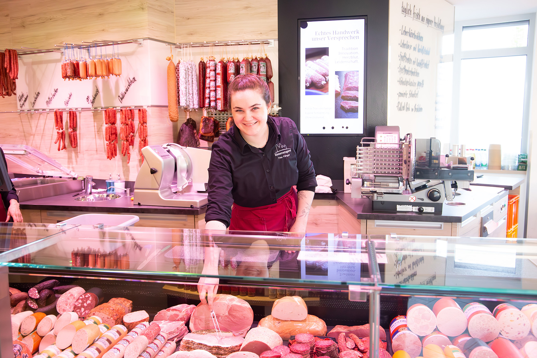 Junge Frau hinter einer Frischetheke sticht mit einer Gabel in eine Wurst
