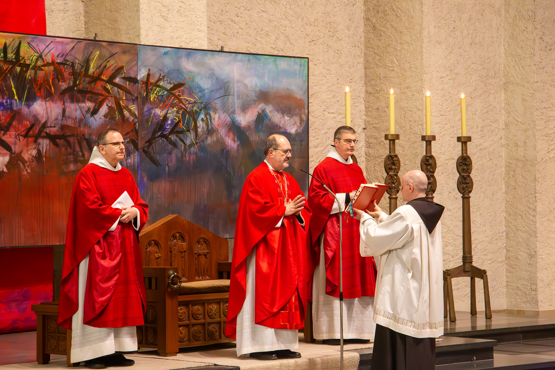 Drei Mönche im roten Gewand, einer liest aus einem Buch