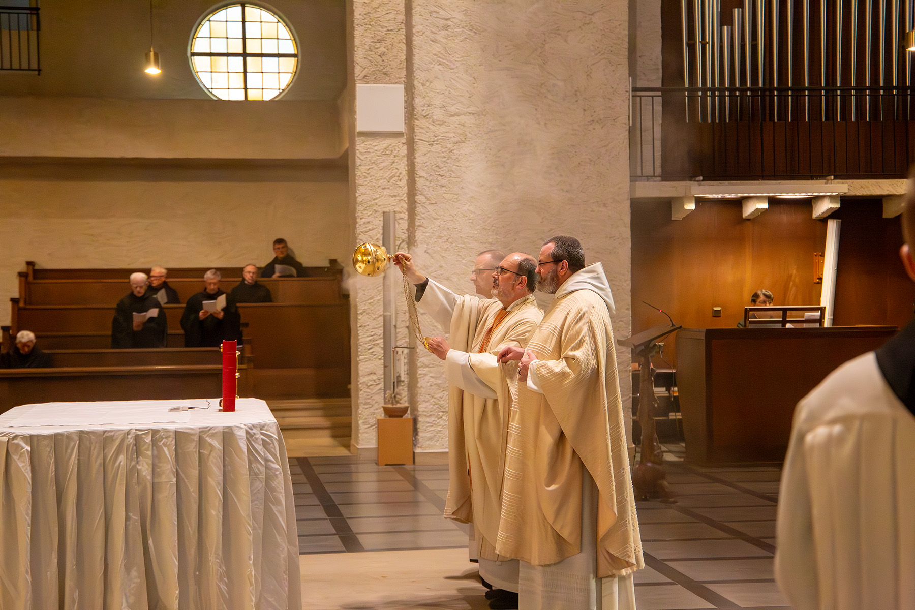 Mönche im Gewand stehen vor Altar und verteilen Weihrauch