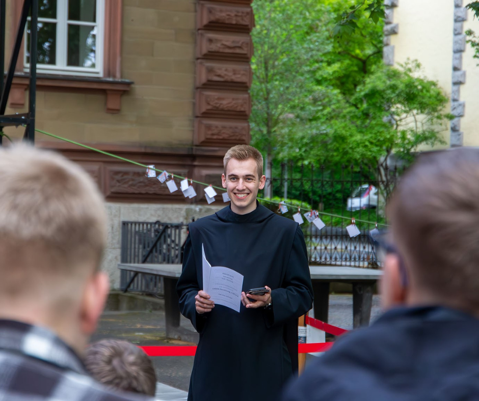 Junger Mönch im Habit mit Zettel und Mikrophon in der Hand