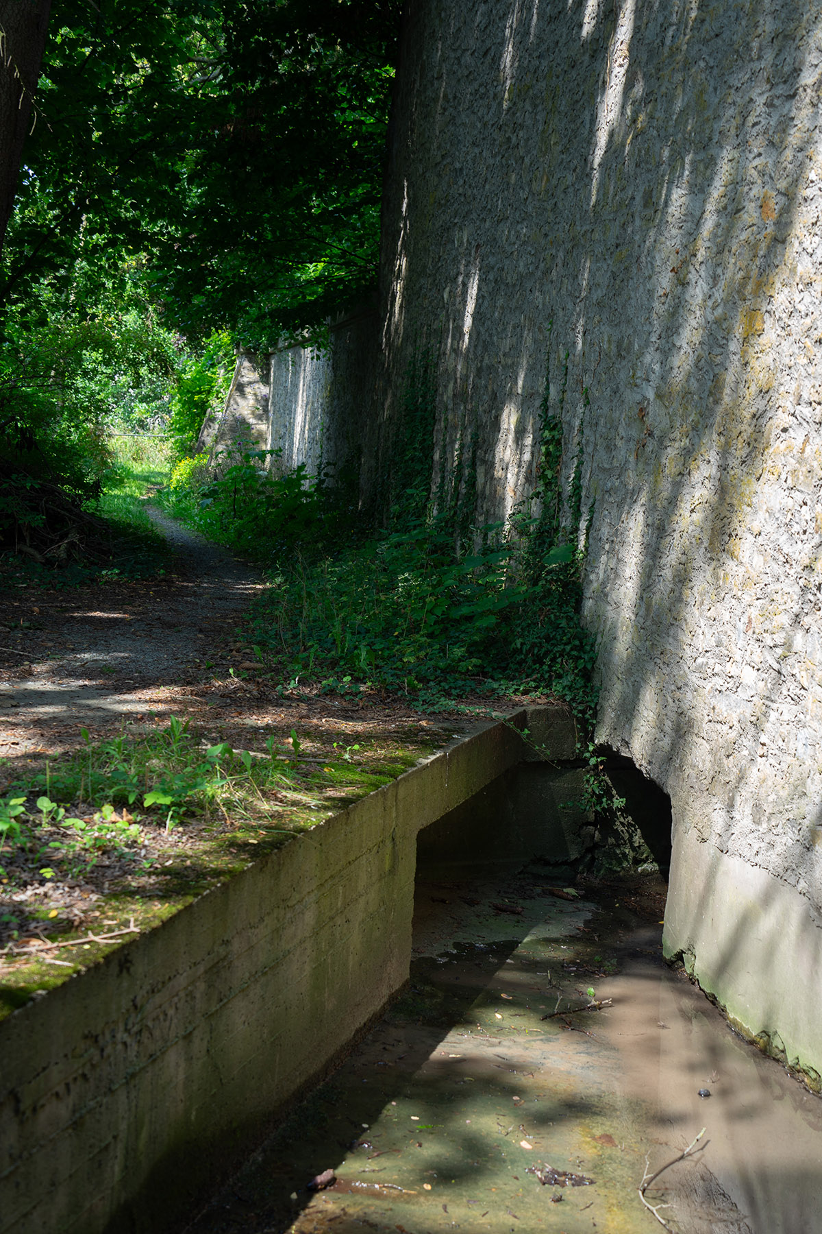 Bach verschwindet in eine Öffnung an einer großen Mauer