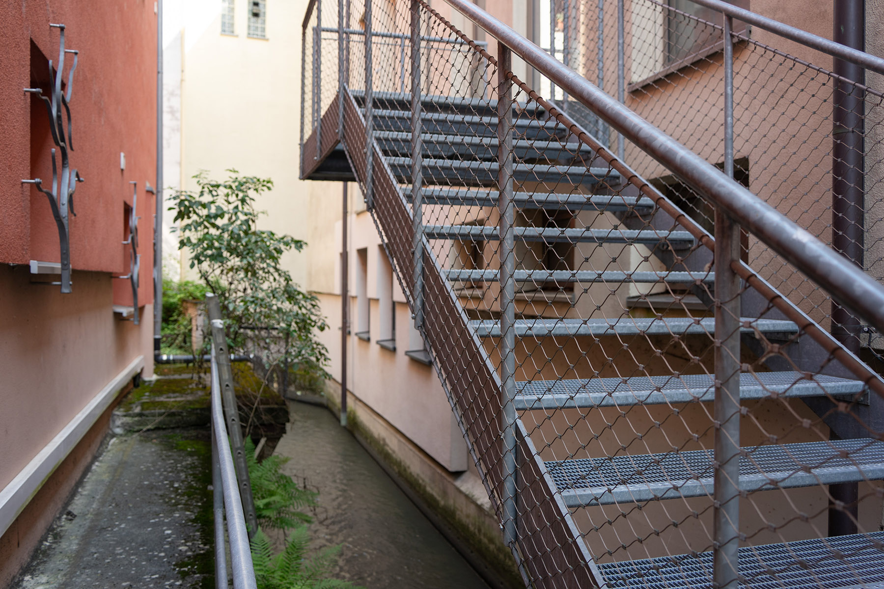 Metalltreppe an einem organfarbigen Gebäude, darunter fließt der Bach