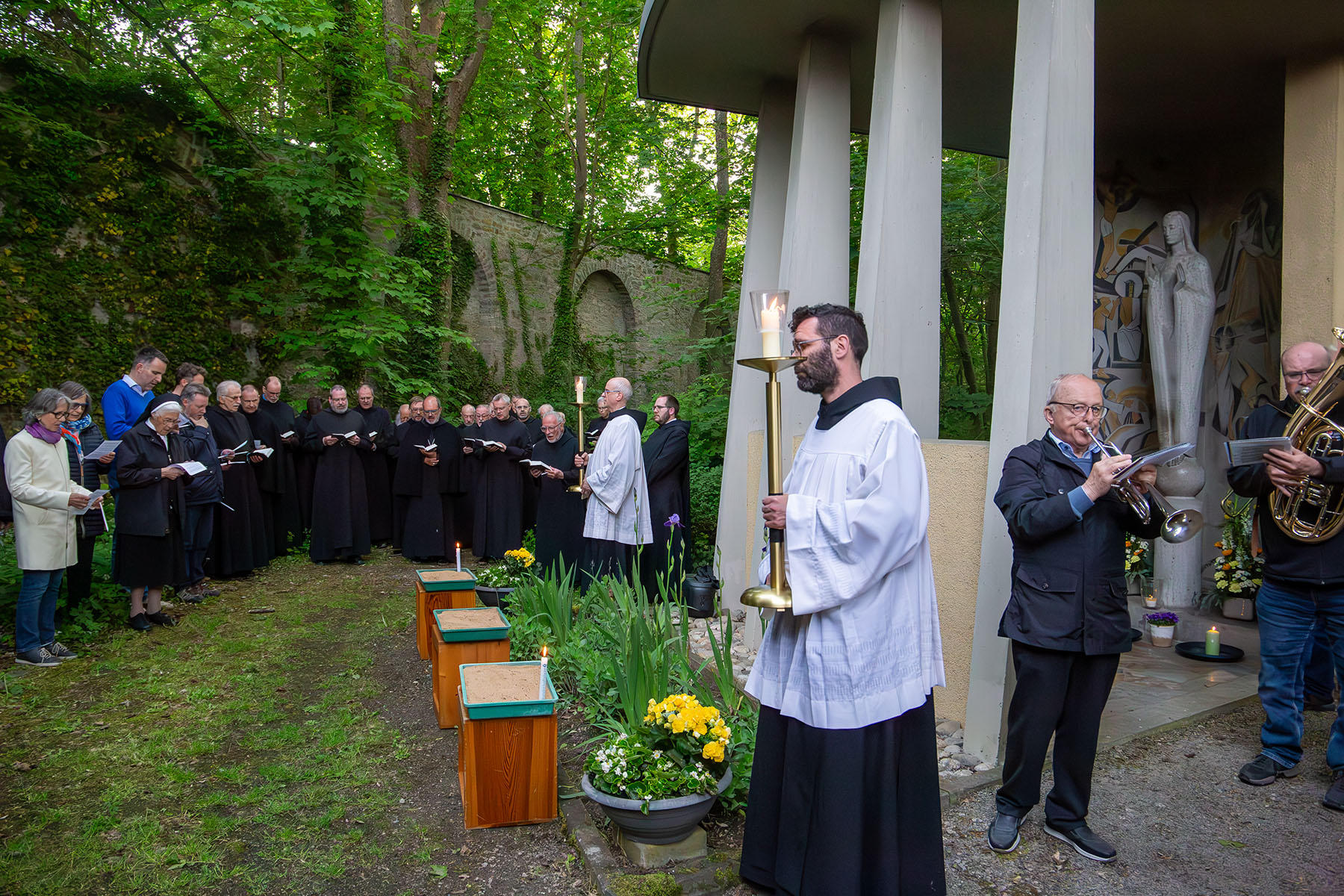 Gruppe von Menschen an der Kapelle, vorne steht Mann im weißen Gewandt mit Kerze
