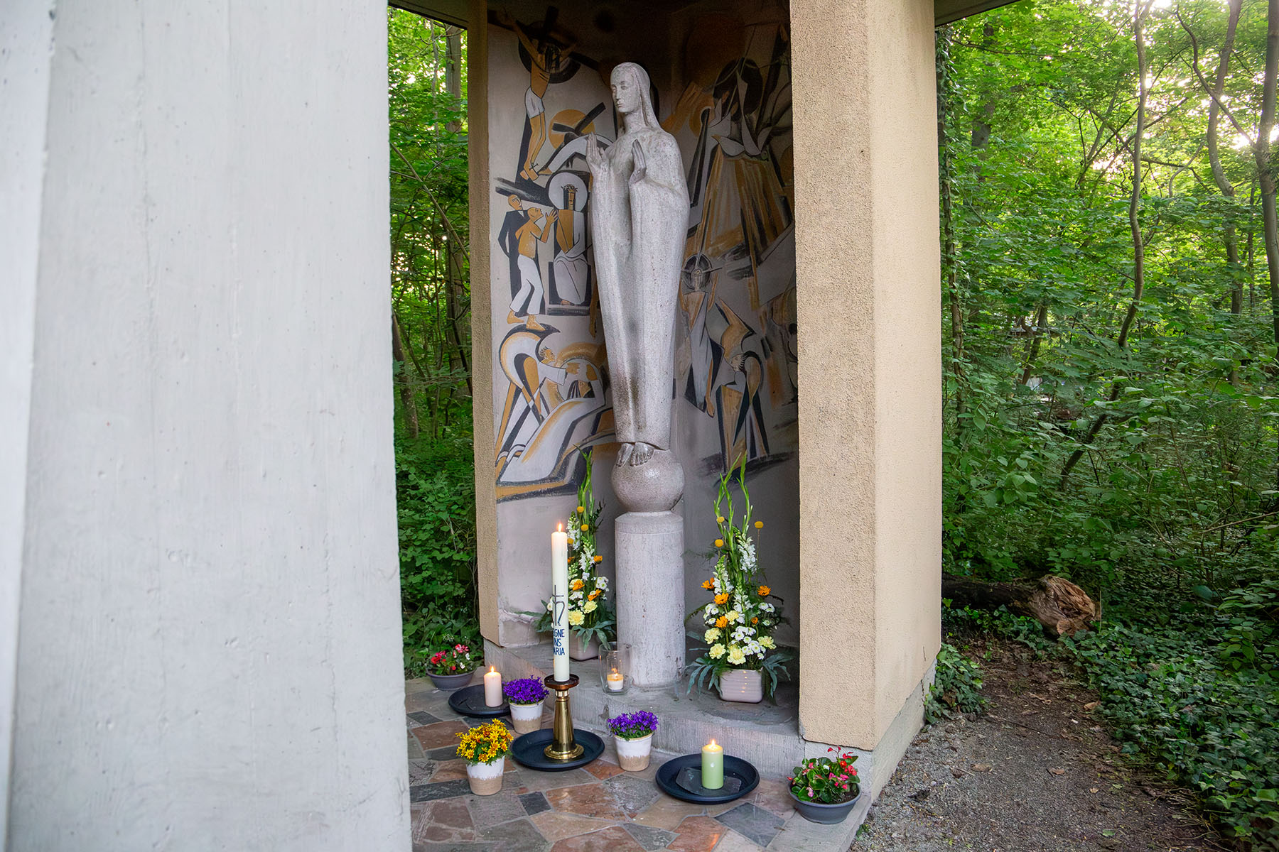 Marienfigur, vor der brennende Kerzen und Blumen stehen