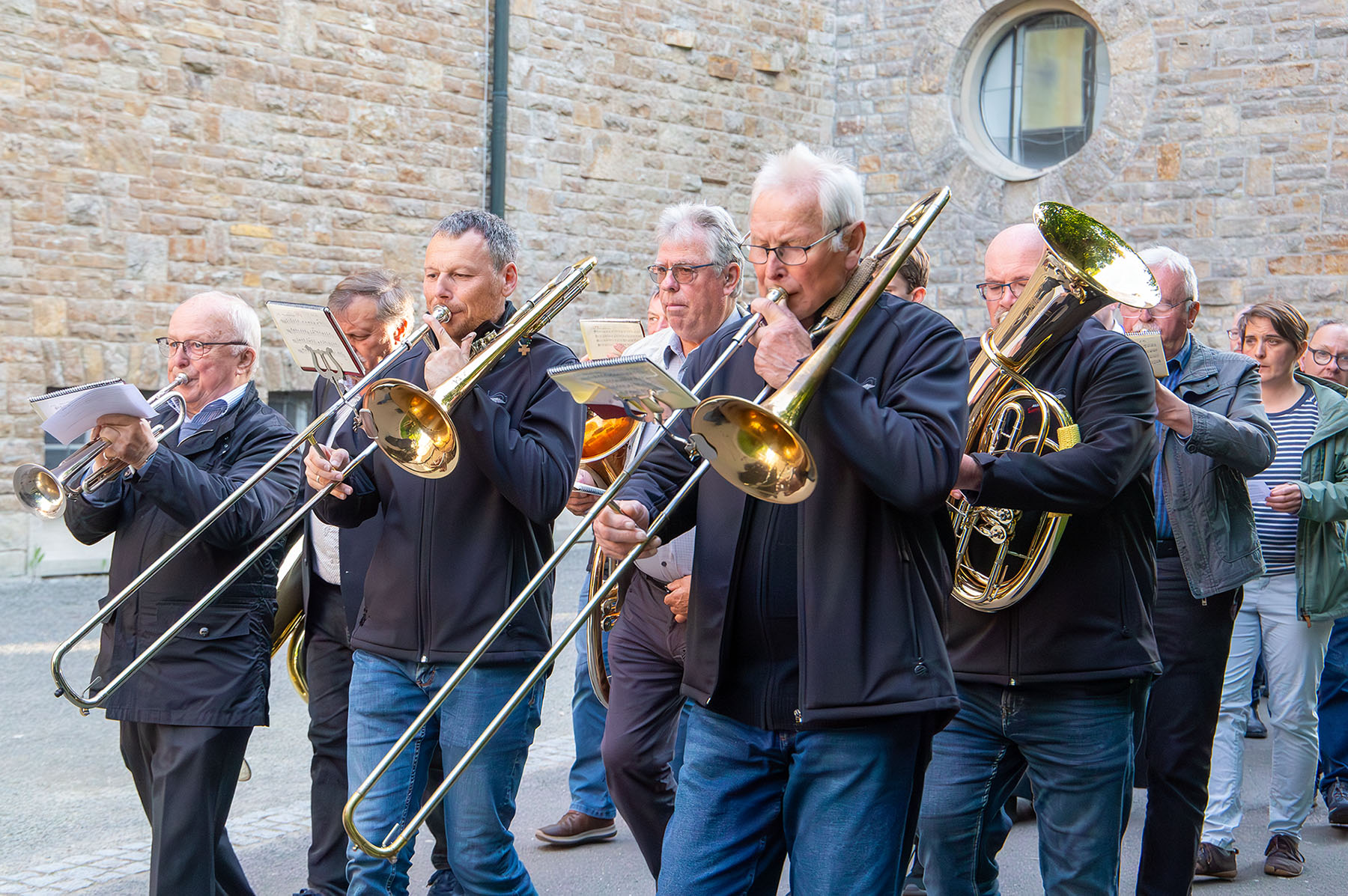 Männer mit Blasinstrumenten vor einer Steinwand