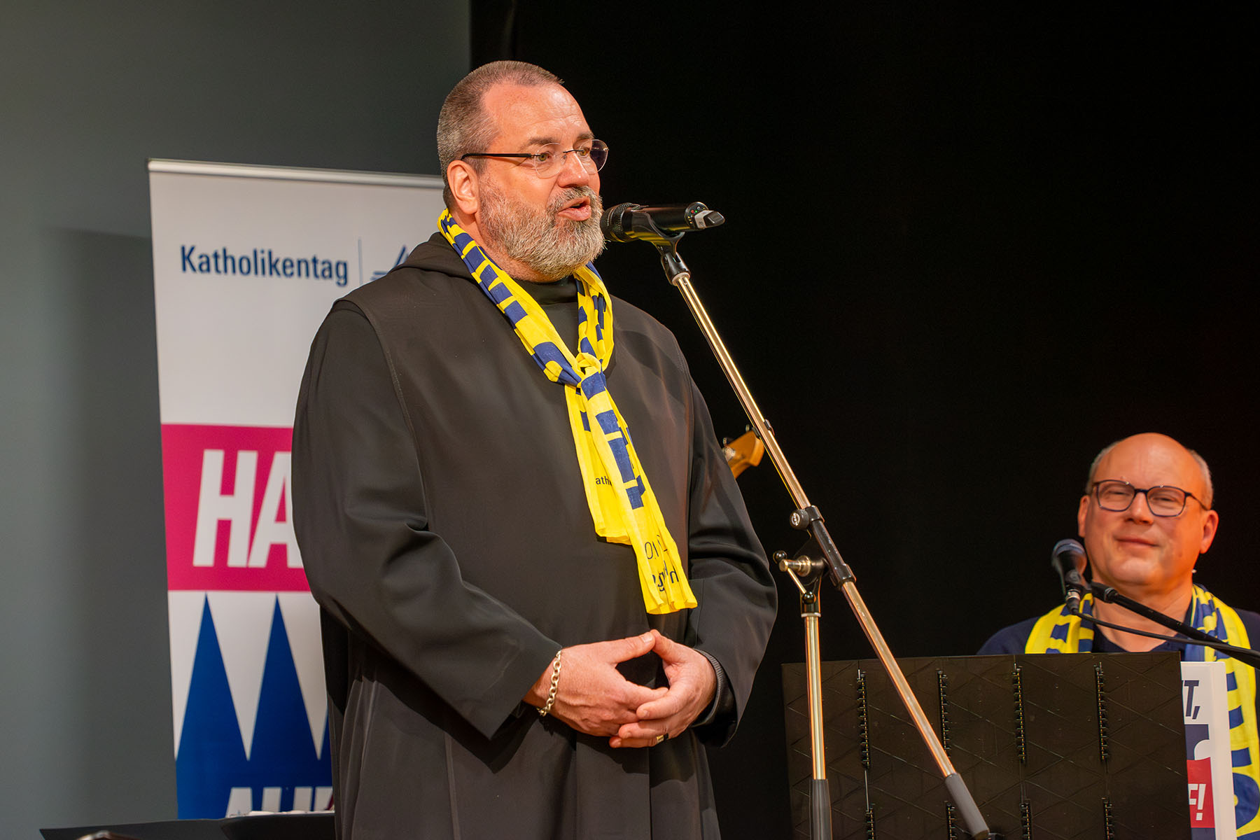 Mönch mit Bart und im Habit auf einer Bühne
