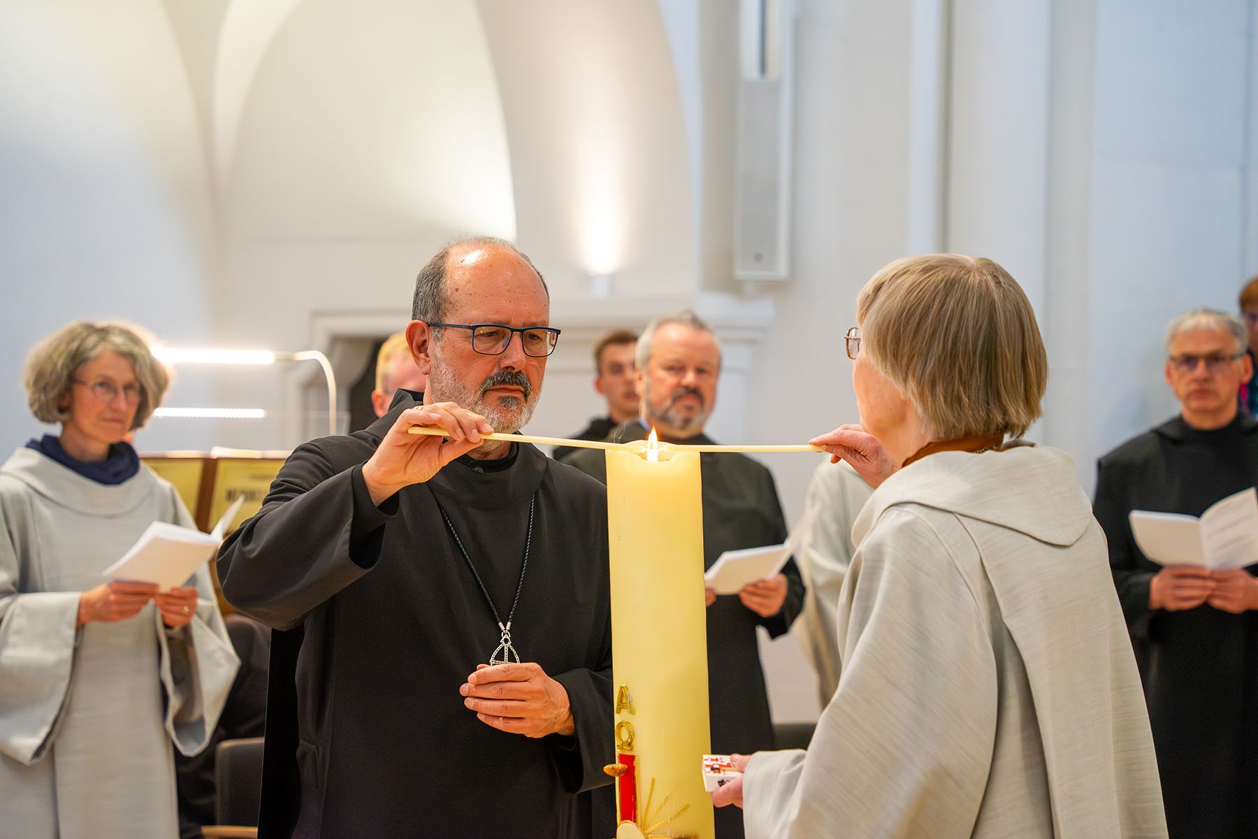 Mönch und Schwester entzünden Kerzen an einer großen Kerze