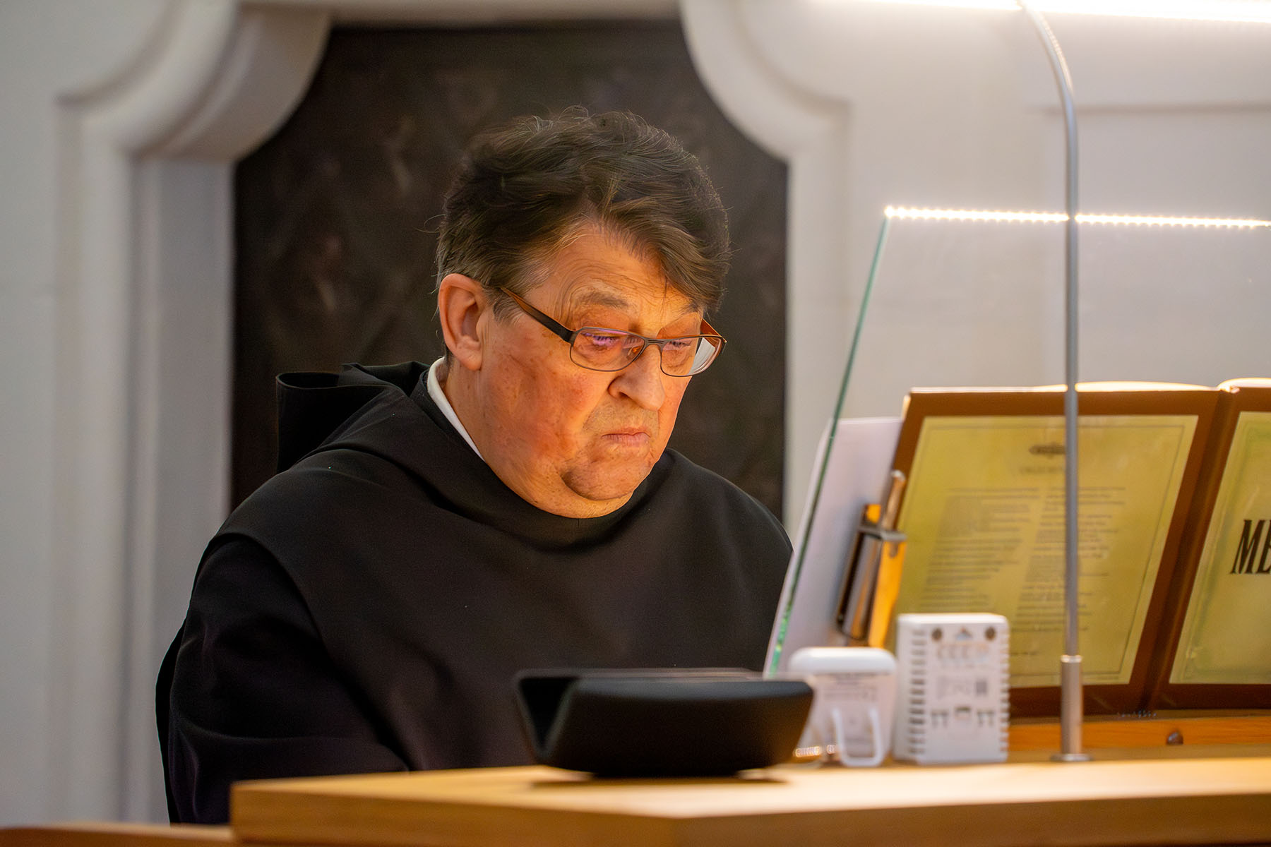 Mönch mit Brille sitzt an einer Orgel