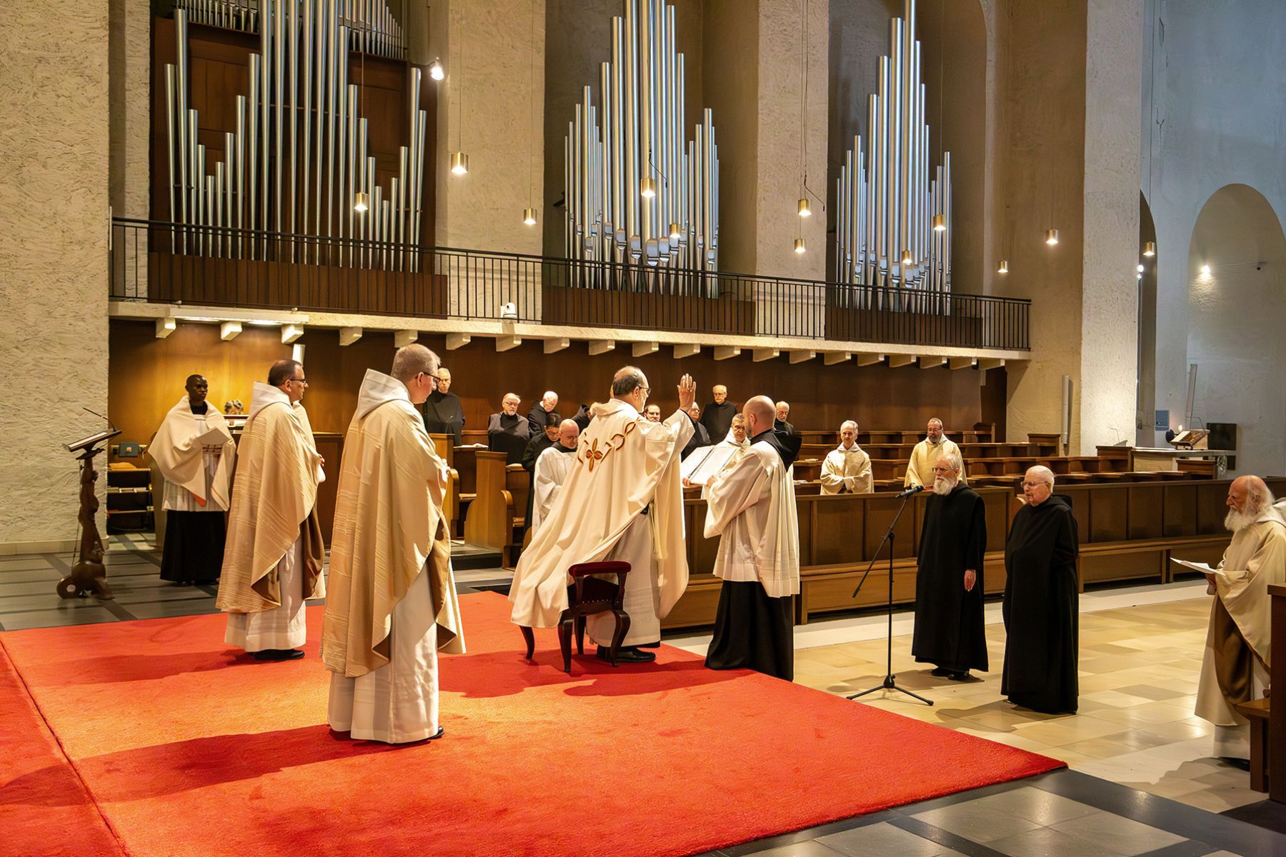 Priester stehen in der Kirche vor einer Orgel, einer der Männer hebt die Hände zum Gebet