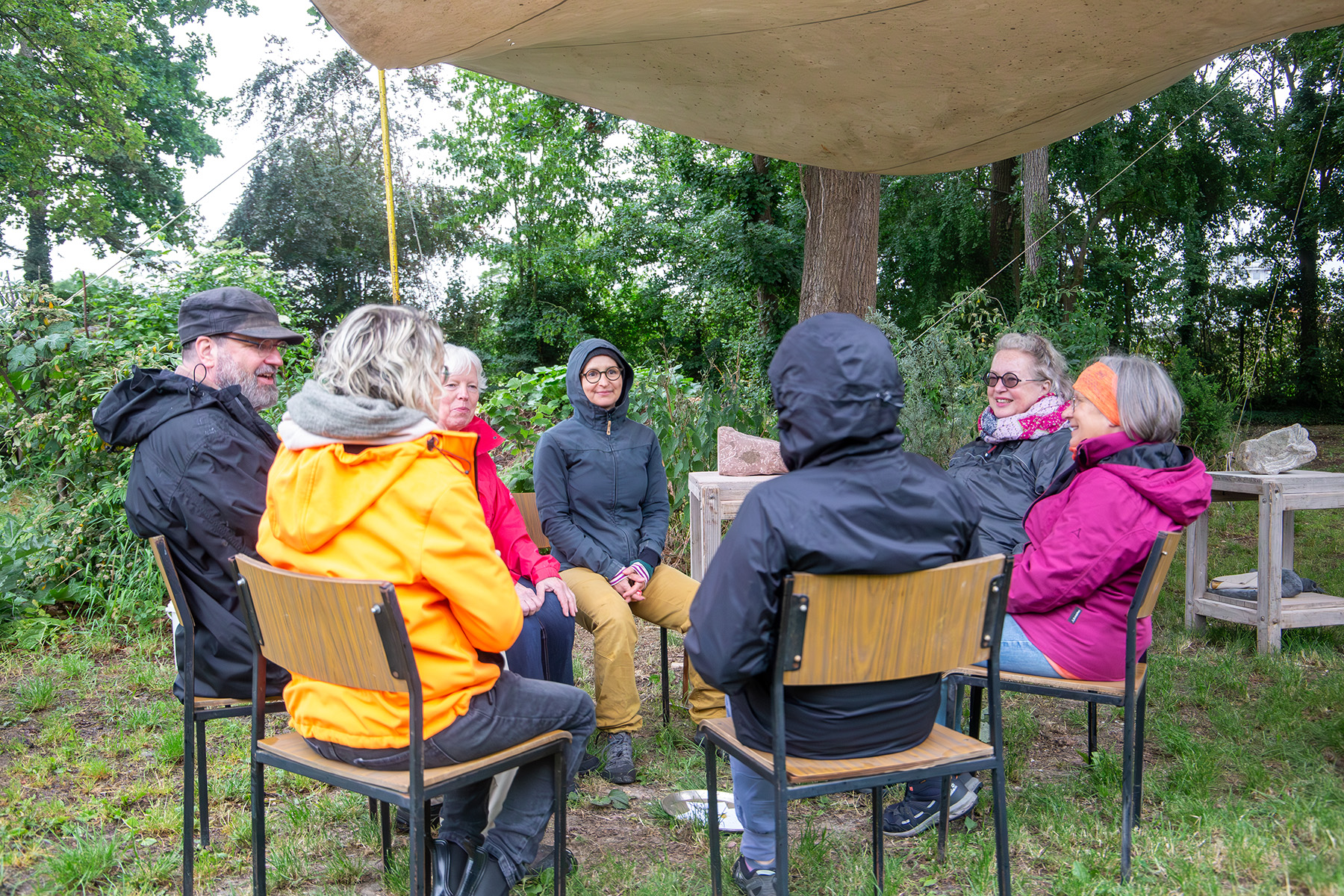 Menschen sitzen auf Stühlen unter einem Sonnensegel auf einer Wiese