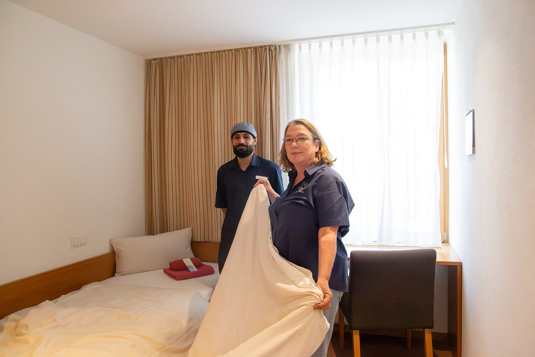 Junger Mann und Frau im Hotelzimmer beim Bettenmachen