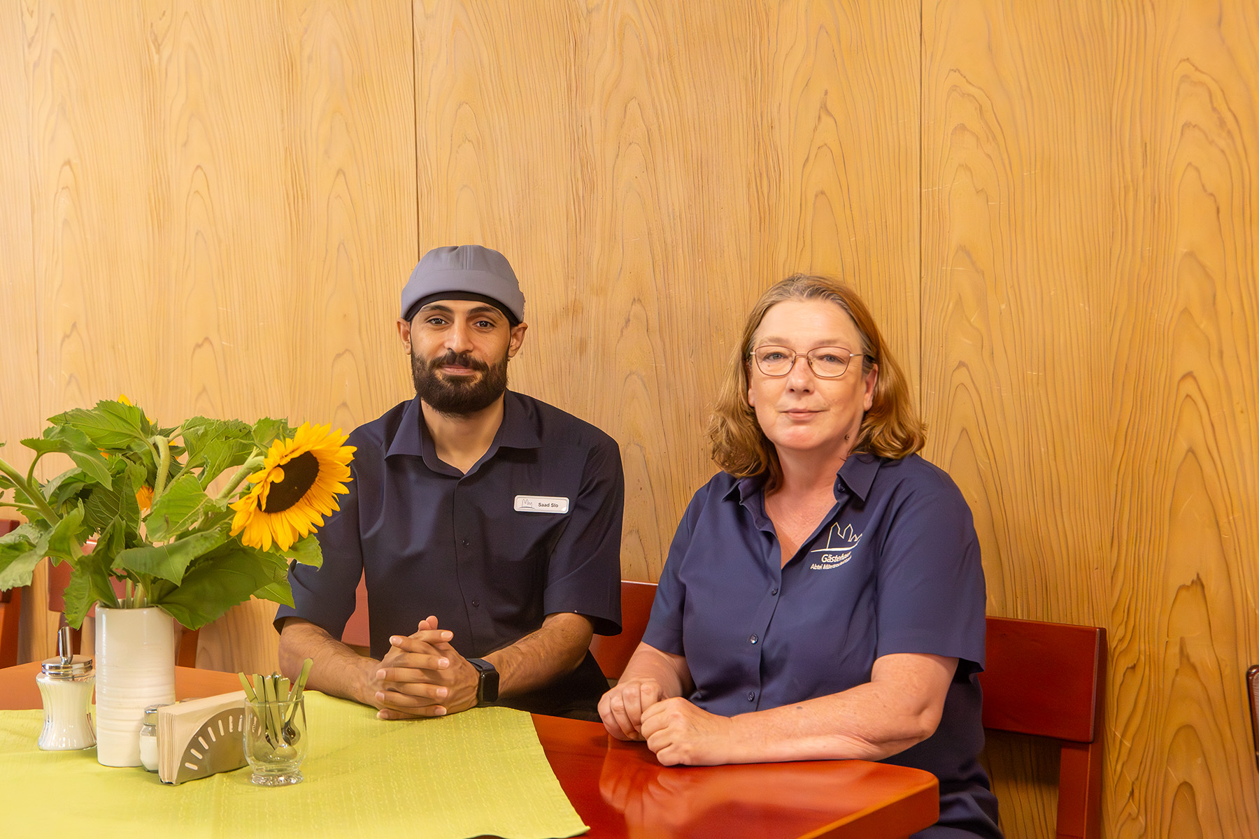Junger Mann und Frau sitzen an einem Tisch mit Sonnenblumenstrauß