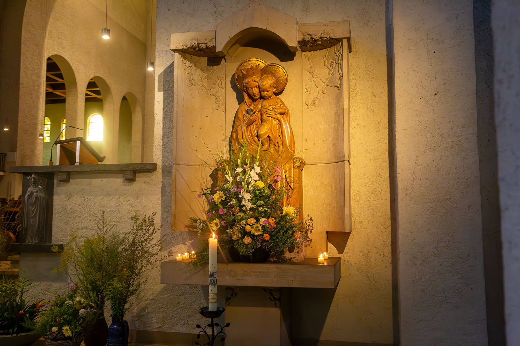 Marienfigur in der Kirche mit brennenden Kerzen und Blumenschmuck