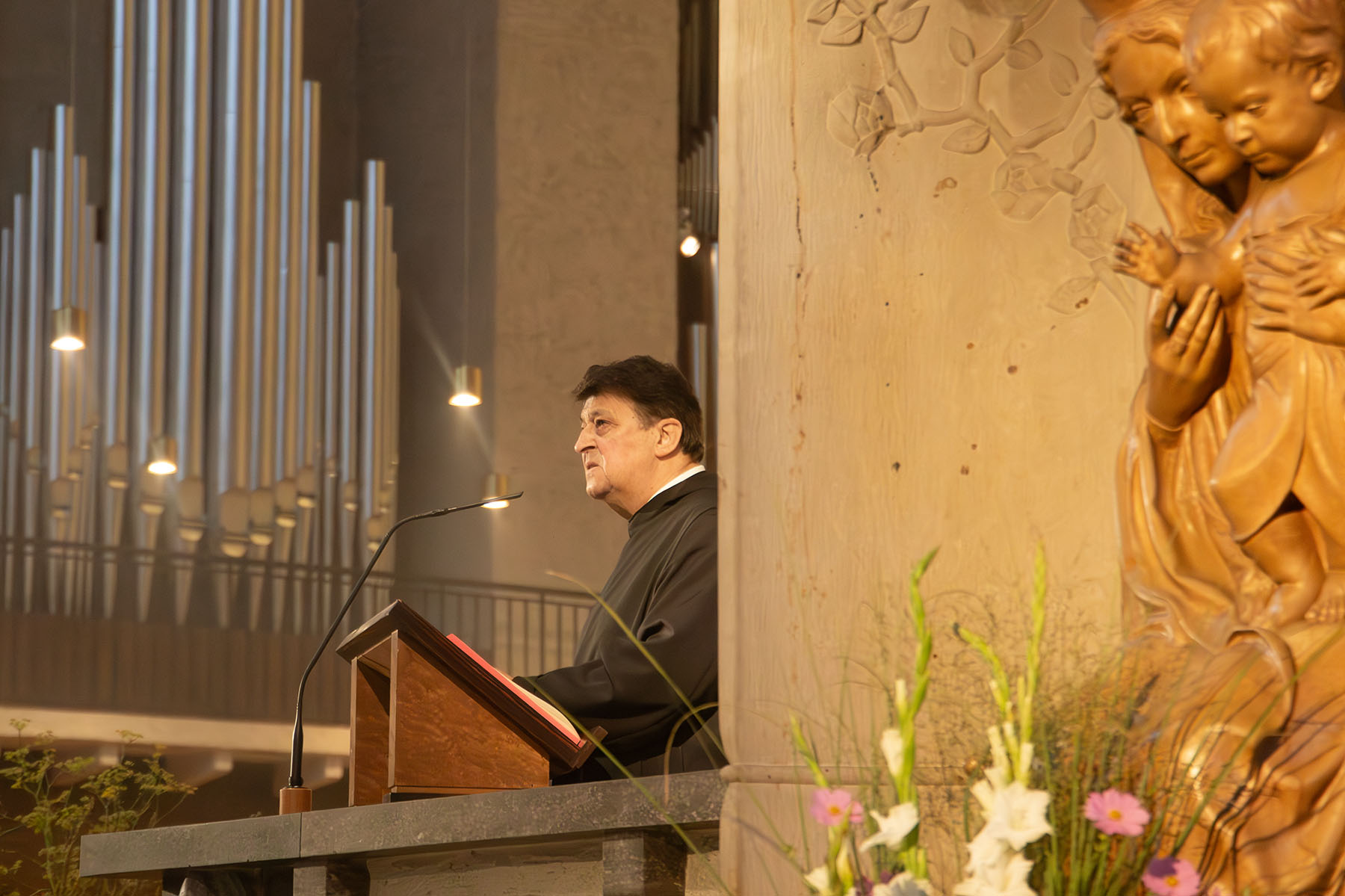 Priester steht an einem Redepult und schaut in die Kirche