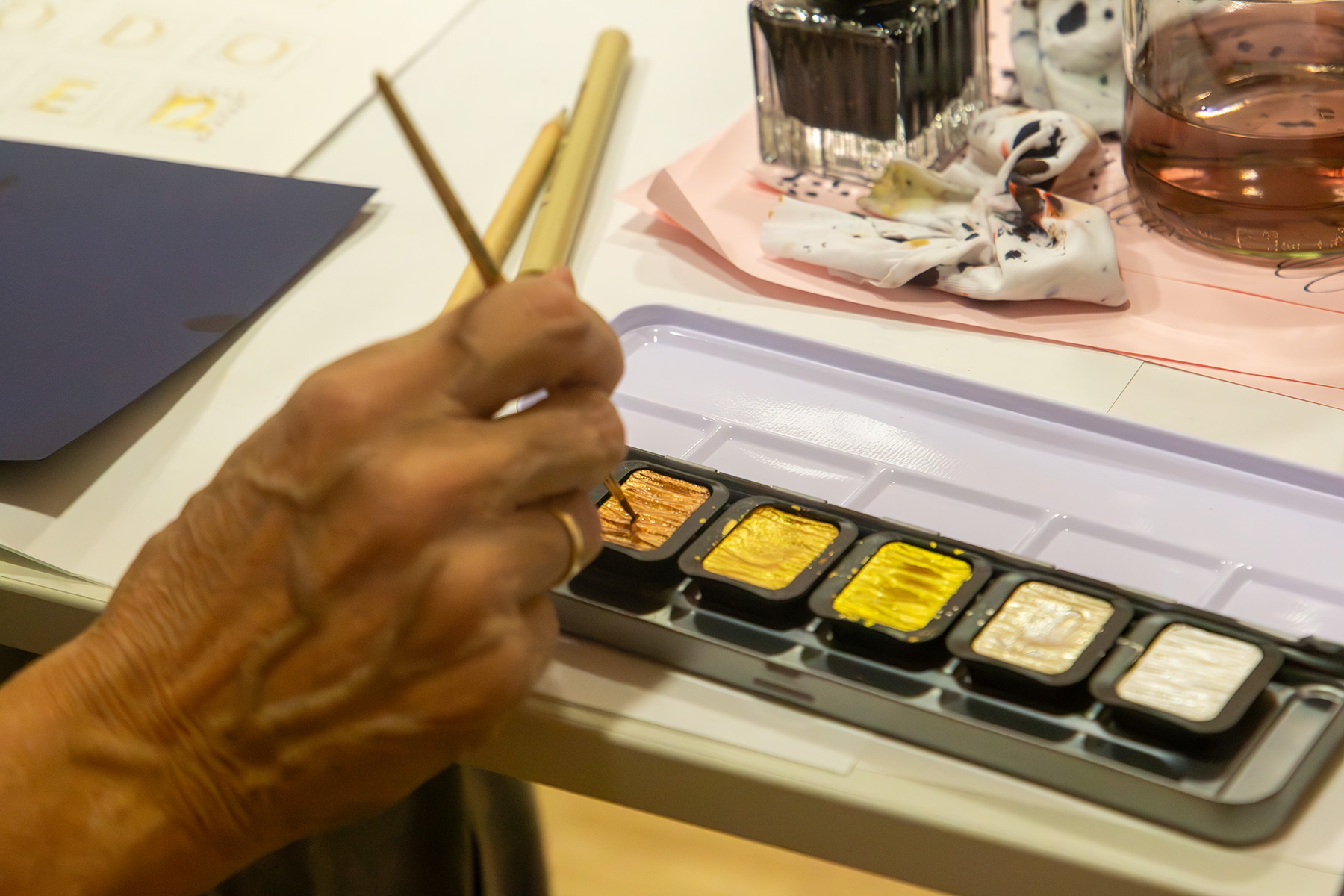 Hand mit einem Pinsel, der in einen Farbkasten taucht