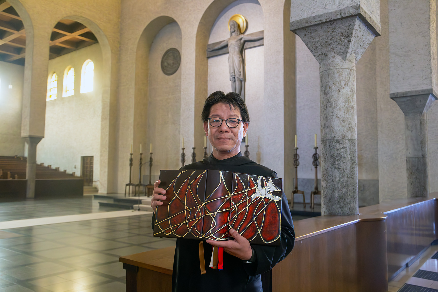 Mönch in schwarzem Gewand hält großes Buch in einer Kirche