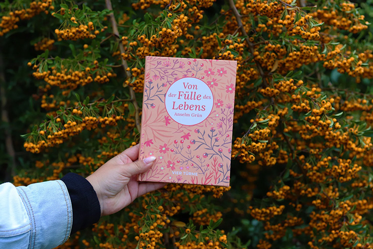 Hand hält ein Buch vor einem Strauch mit orangen Beeren