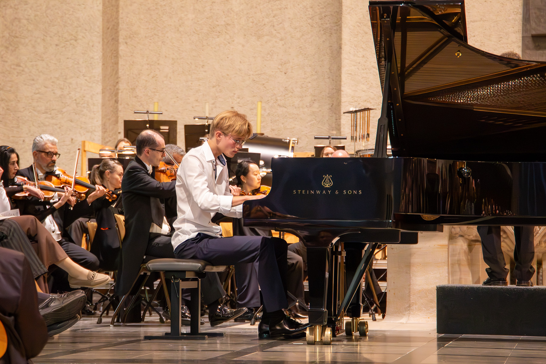 Junger Mann spielt am Klavier, dahinter ist das Orchester
