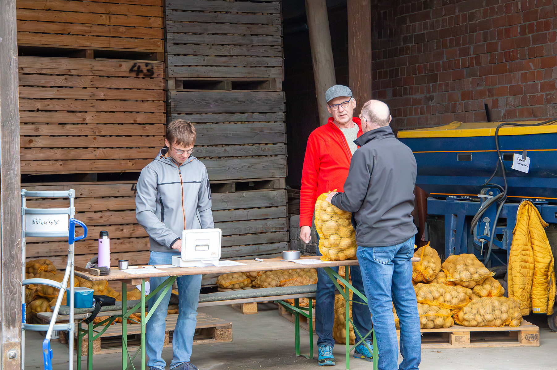 Drei Männer stehen an Verkaufsstand mit Kartoffeln