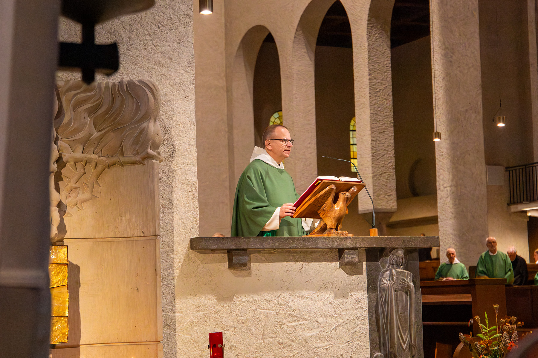 Priester steht auf Kanzel und liest aus einem großen Buch