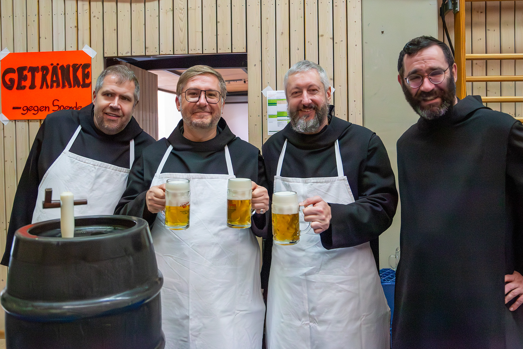 Vier Mönche, zwei davon halten ein Bier hoch