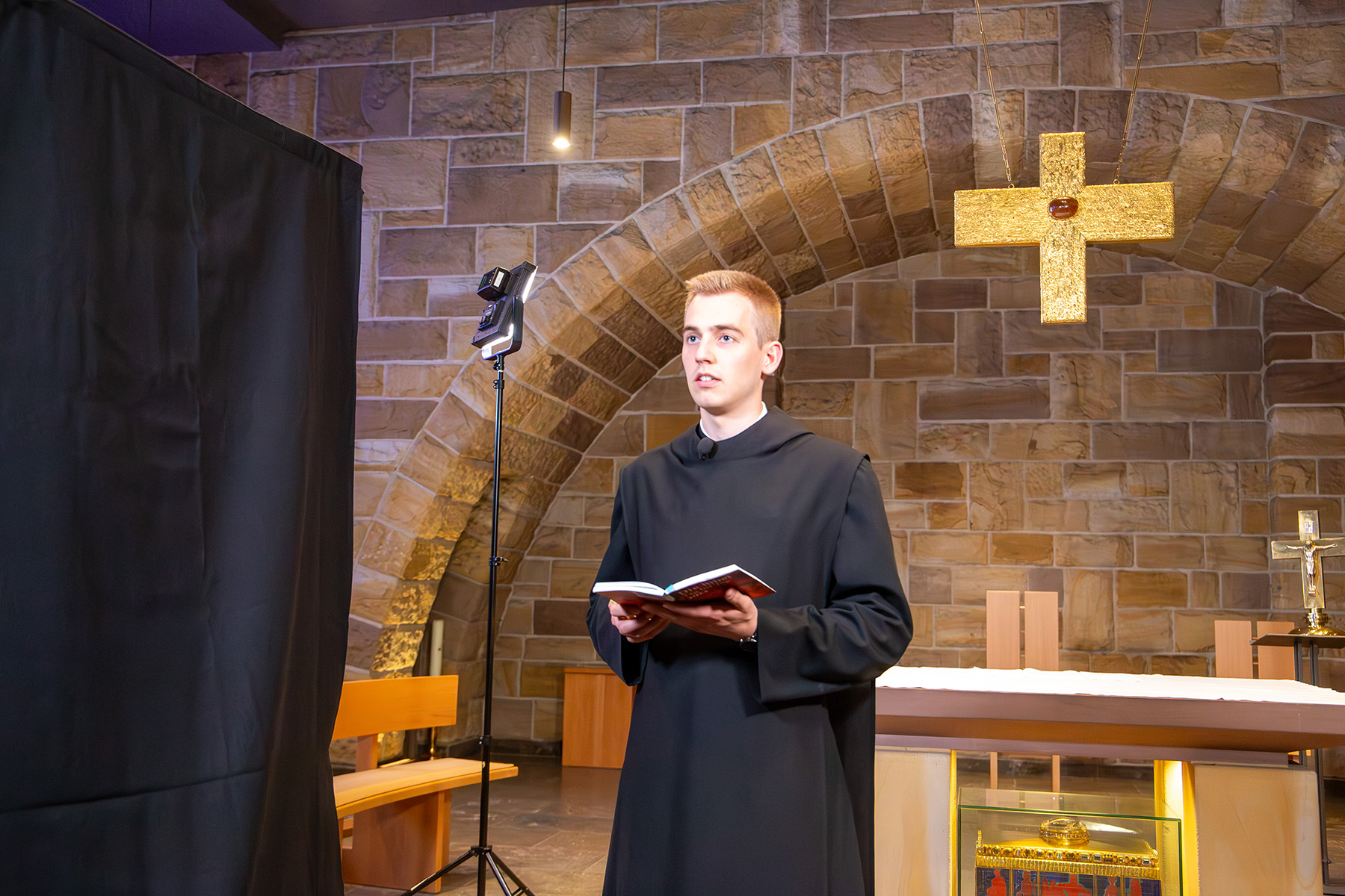 Junger Mönch mit Buch in der Hand vor einem Tischaltar