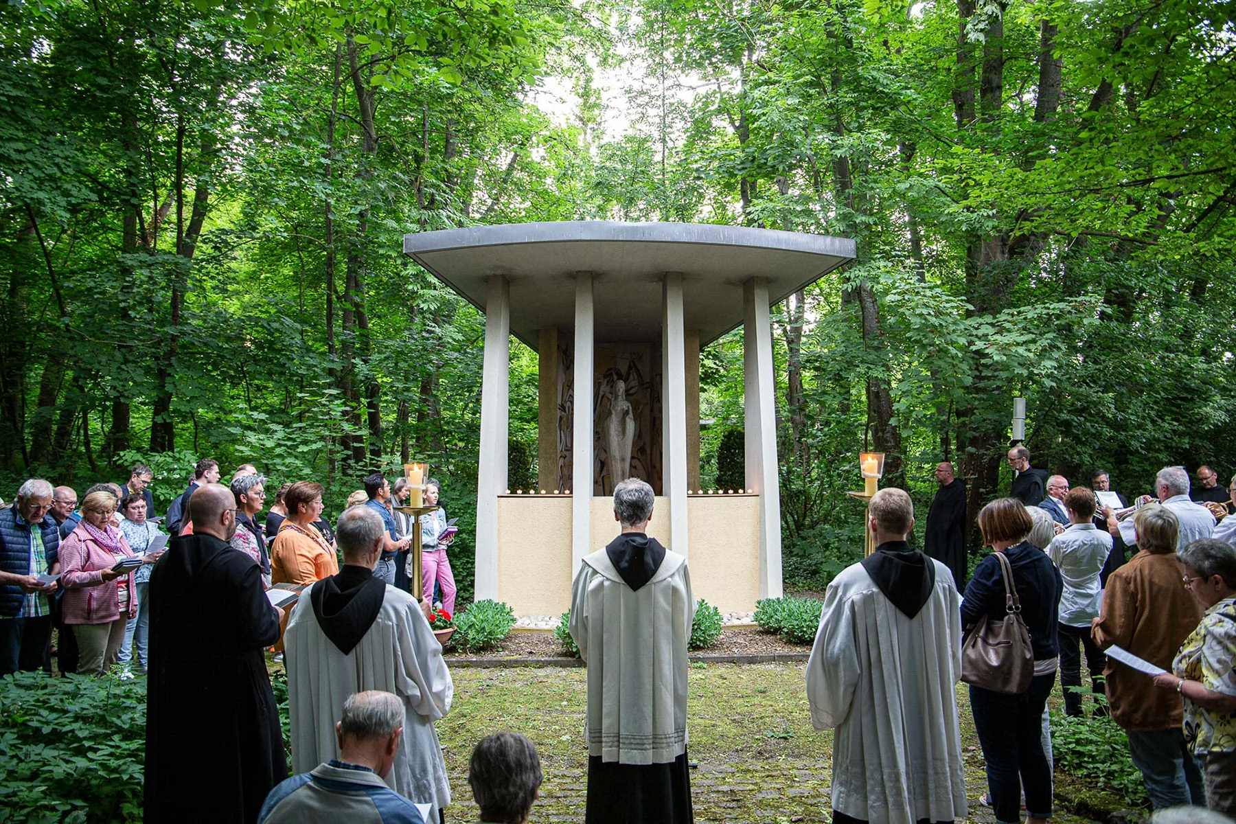 Gruppe von Menschen steht vor einer Marienkapelle in einem Park