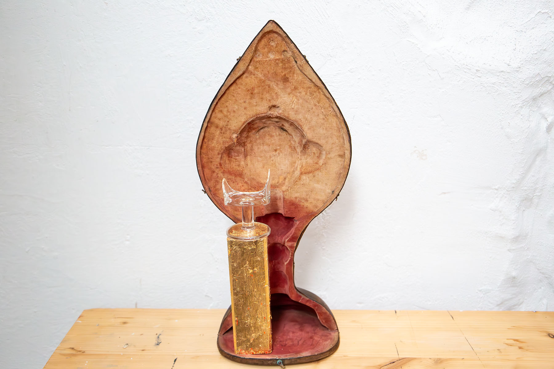 Zerbrochenes Glas auf einem Goldsockel vor einem Kelchkoffer