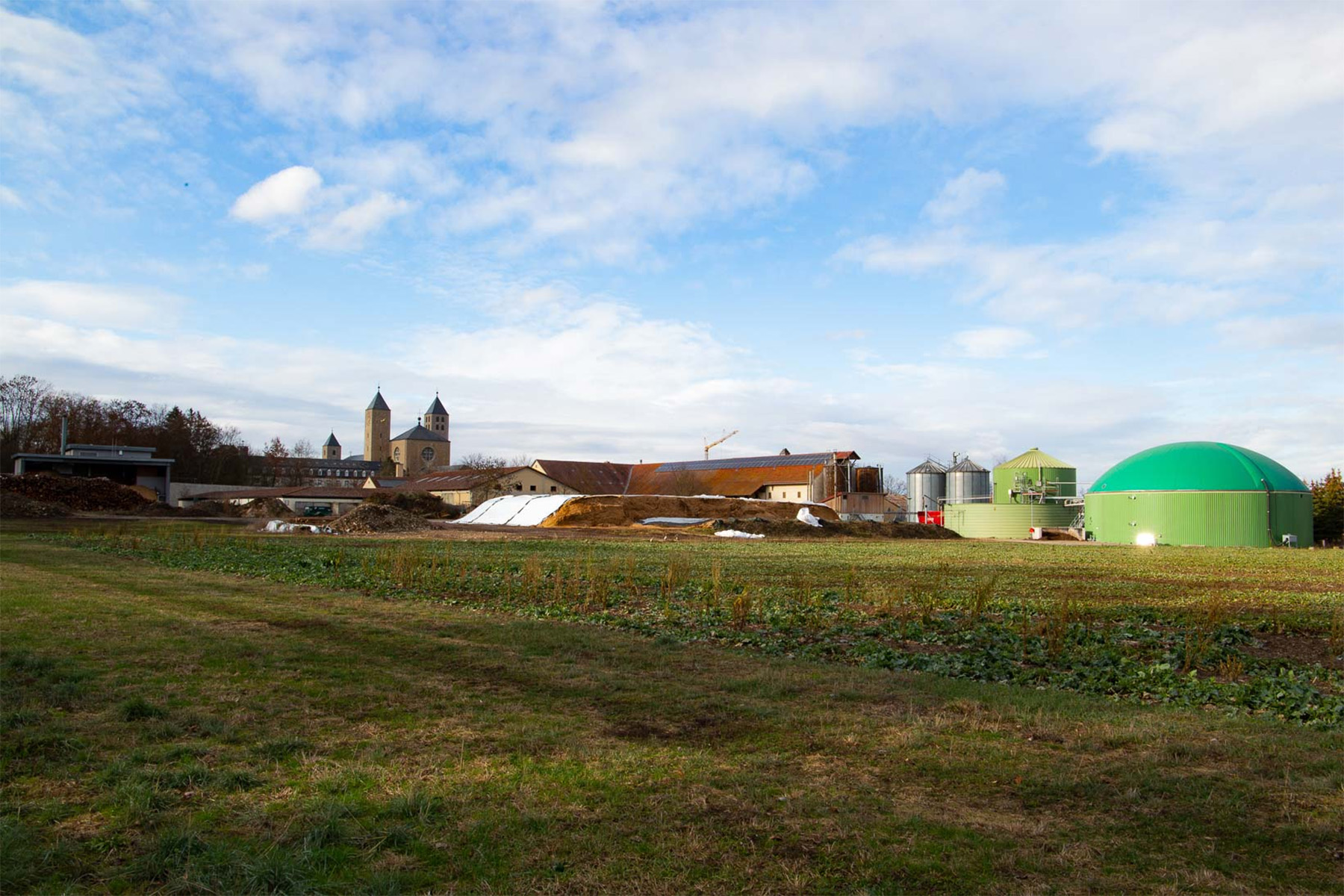 Blick auf eine Biogasanlage, im Hintergrund sieht man Kirchtürme