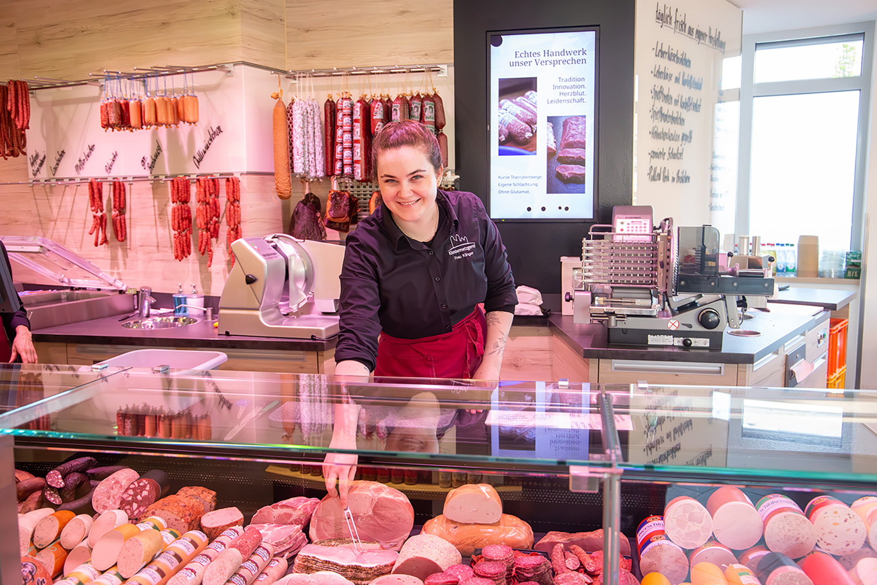 Junge Frau greift mit Gabel in Wursttheke