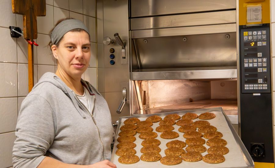 Frau steht mit Blech voller Lebkuchen vor einem großen Backofen