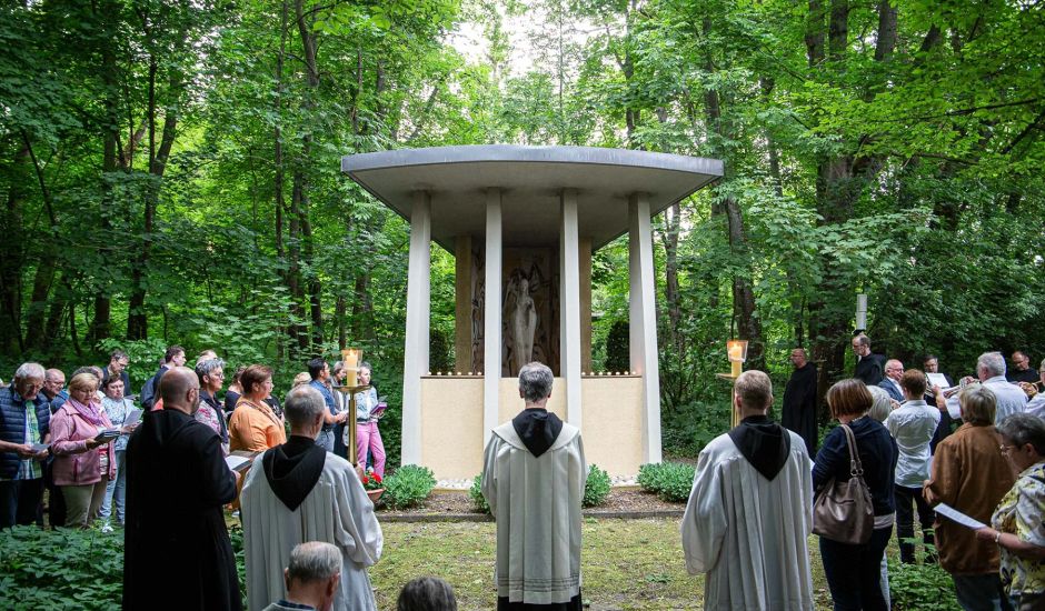 Gruppe von Menschen steht vor einer Marienkapelle in einem Park