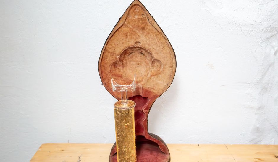 Zerbrochenes Glas auf einem Goldsockel vor einem Kelchkoffer