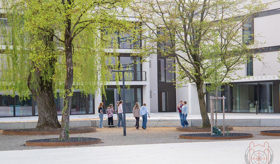 Blick auf ein Schulgebäude, vor dem Jugendliche sowie mehrere Bäume stehen