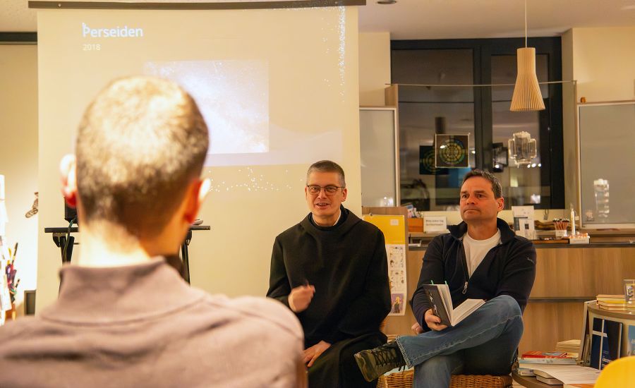 Mann im Habit und Mann in Alltagskleider sitzen in einem Buchladen