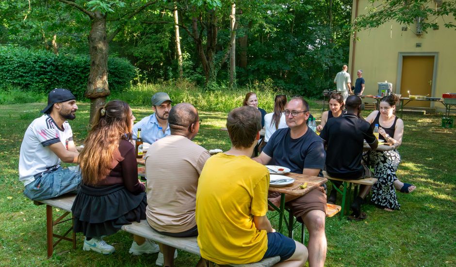 Eine Gruppe junger Mitarbeitender sitzt auf einer Biertischgarnitur im Grünen