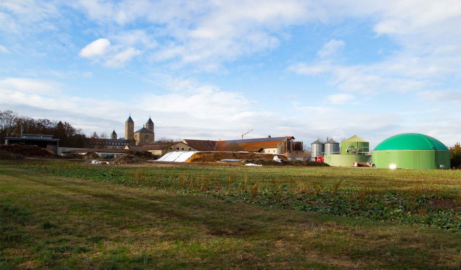 Blick auf eine Biogasanlage, im Hintergrund die Türme einer Kirche