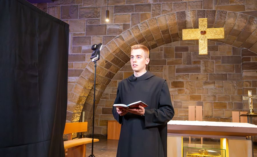 Junger Mönch mit Buch in der Hand vor einem Tischaltar