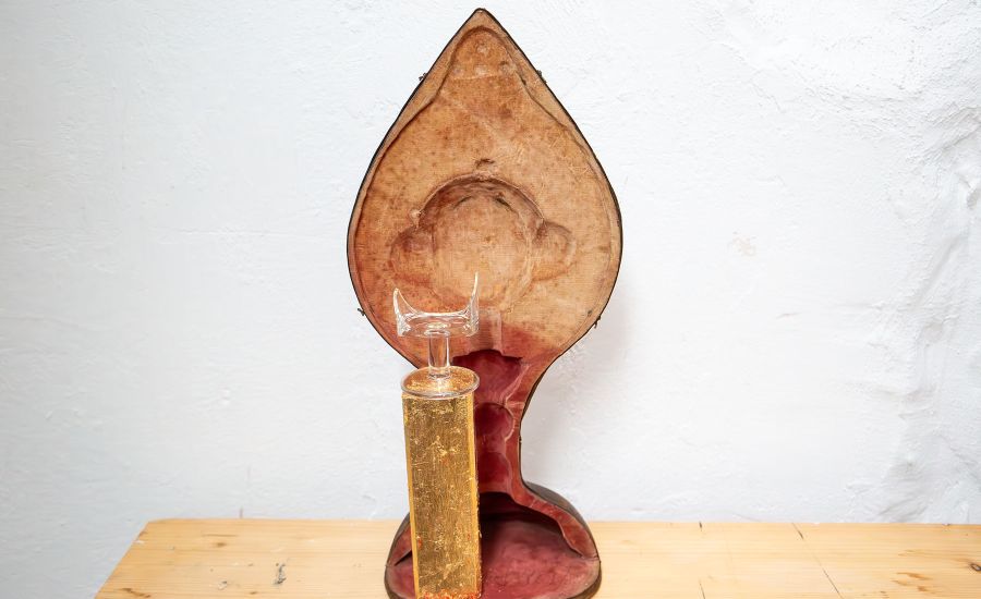 Zerbrochenes Glas auf einem Goldsockel vor einem Kelchkoffer
