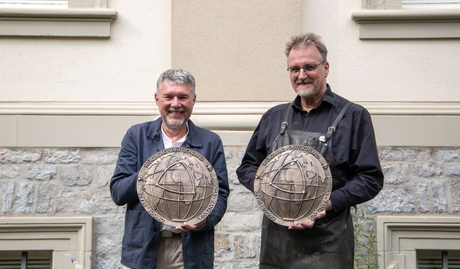 Zwei Männer vor Gebäude, beide halten eine groß Bronzeplakette in der Hand