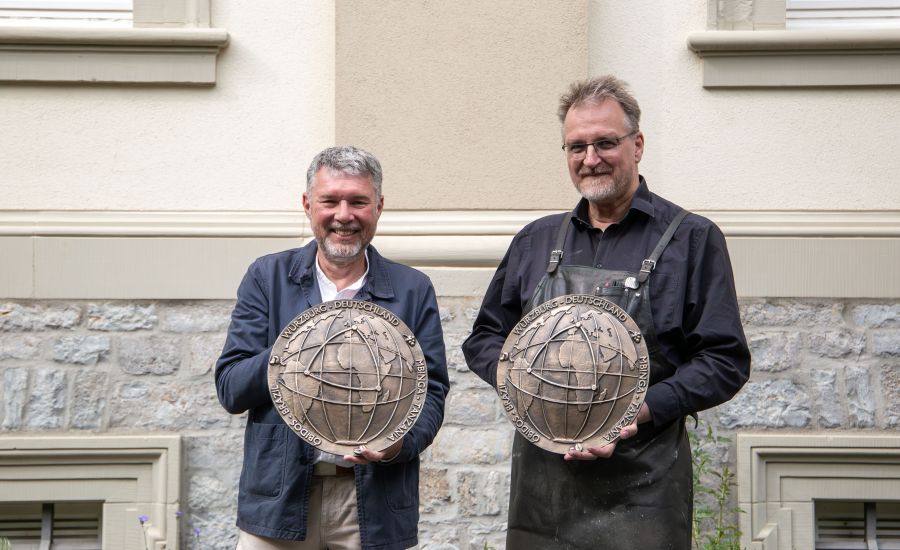 Zwei Männer vor Gebäude, beide halten eine groß Bronzeplakette in der Hand
