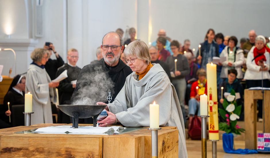Mönch und Schwester vor rauchendem Behältnis am Altar