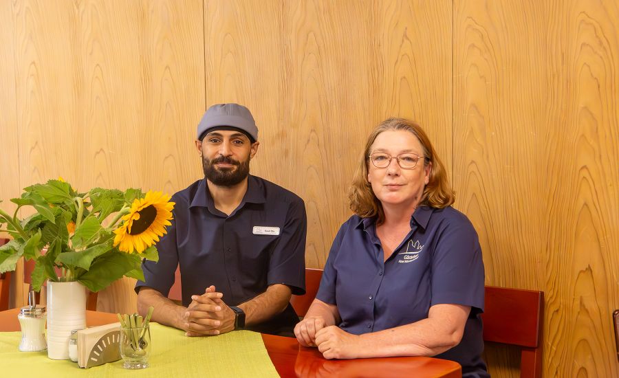 Azubi Saad und Ausbildungsleiterin Anja sitzen an einem Tisch mit Sonnenblumenstrauß