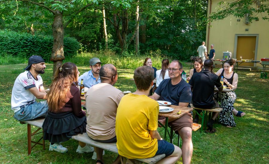Eine Gruppe junger Mitarbeitender sitzt auf einer Biertischgarnitur im Grünen
