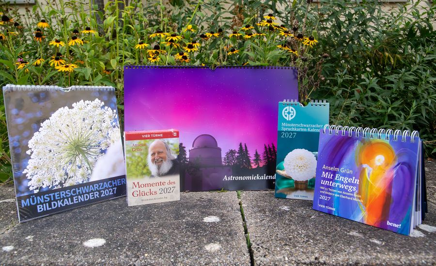 Fünf Kalender für 2027 auf einer Betonfläche, daher sind gelbblühende Blumen