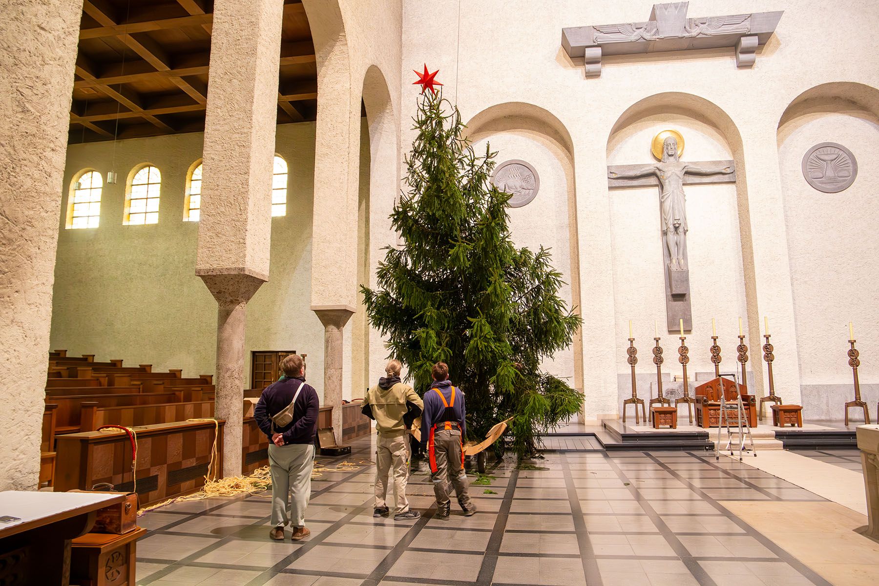 Drei Männer vor dem Tannenbaum, der in der Kirche aufgerichtet wird